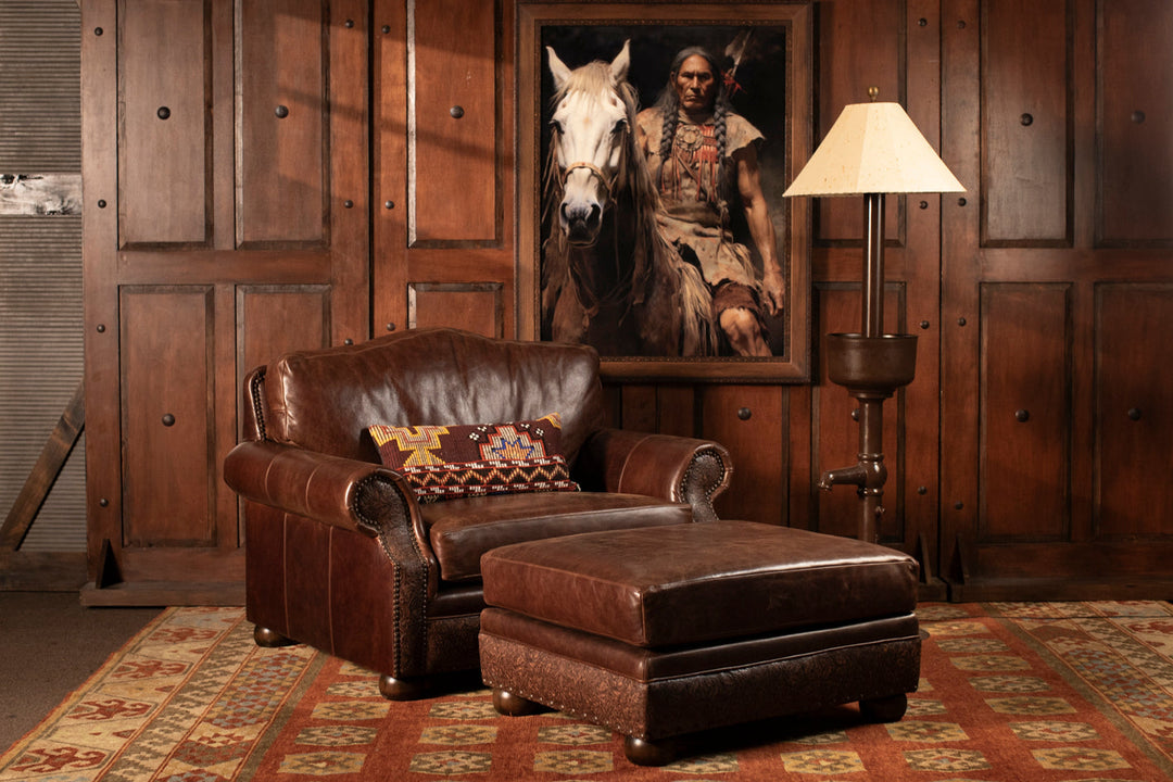 Western-style leather chair and ottoman with embossed base, rustic floor lamp, and Native American artwork in a warm-toned lodge setting.