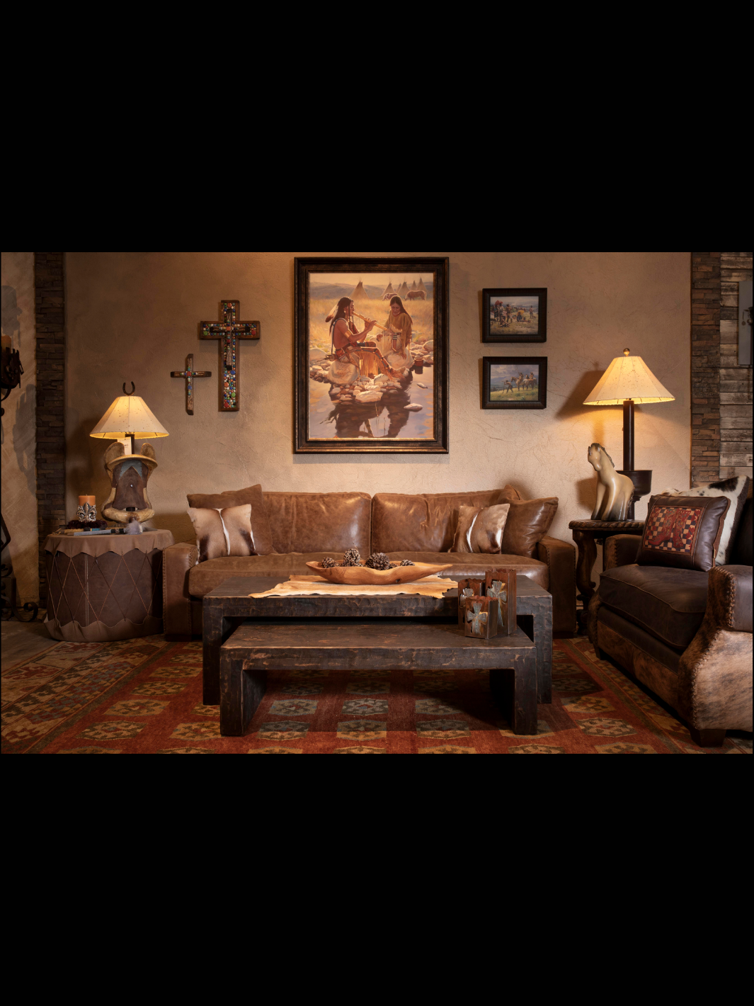 Rustic Western living room with leather sofa, carved wood coffee table, iron cross wall art, Native American paintings, and Southwestern rug.