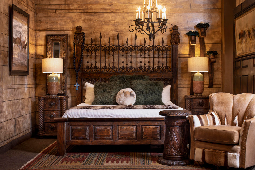 Rustic Western bedroom featuring a hand-carved wood and iron bed, Southwestern flatweave rug, hair-on-hide accent chair, carved wood side table, and textured pillows with warm lighting