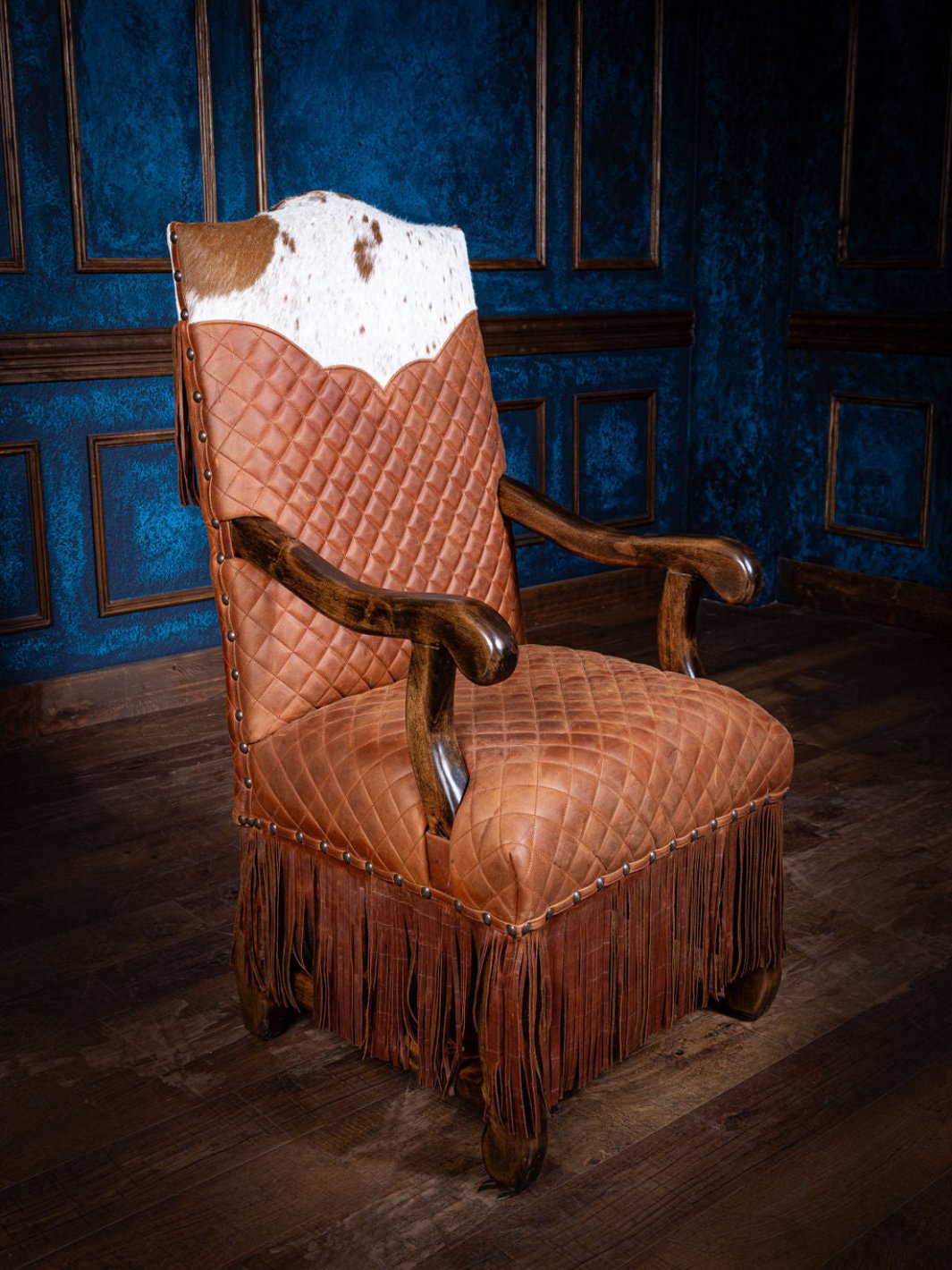 A quilted leather armchair with fringe details, featuring a diamond-quilted pattern on the seat and backrest, and a cowhide yoke on the back. The armchair is displayed against a blue panel background.