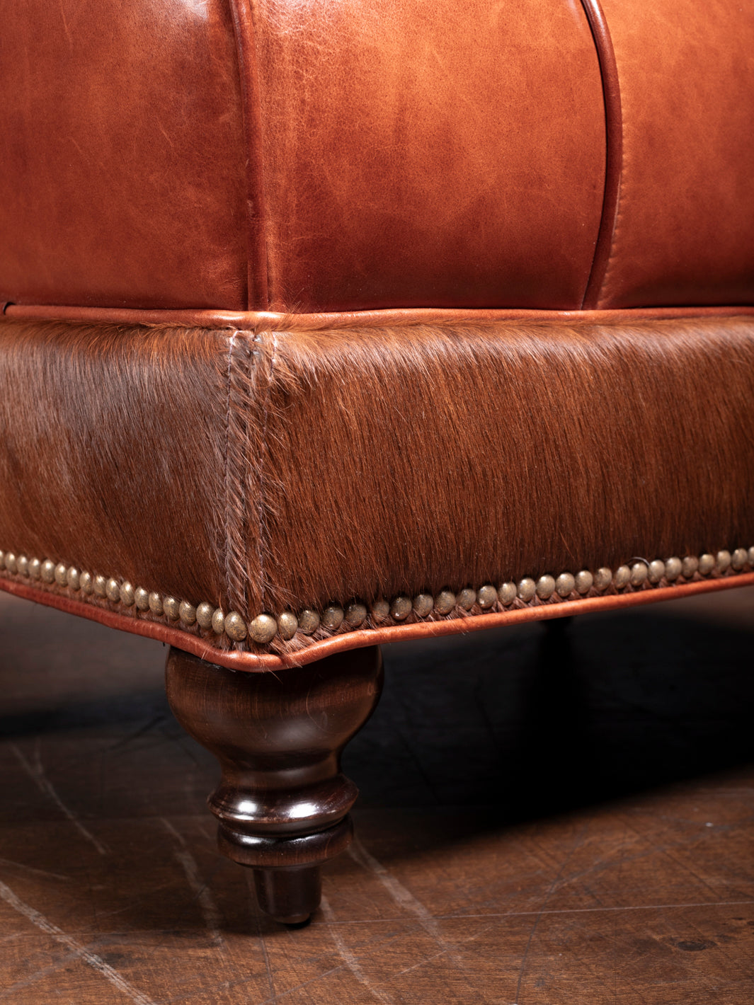 Close-up of the elegant brass nailhead trim and polished wood legs on the Amarillo Red Stitch Ottoman, showcasing its fine craftsmanship.