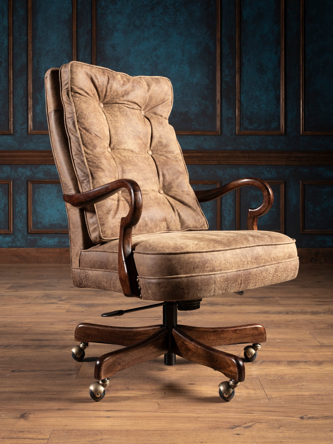 An upholstered brown leather desk chair with a tufted backrest, cushioned seat, wooden arms, and antique brass casters.