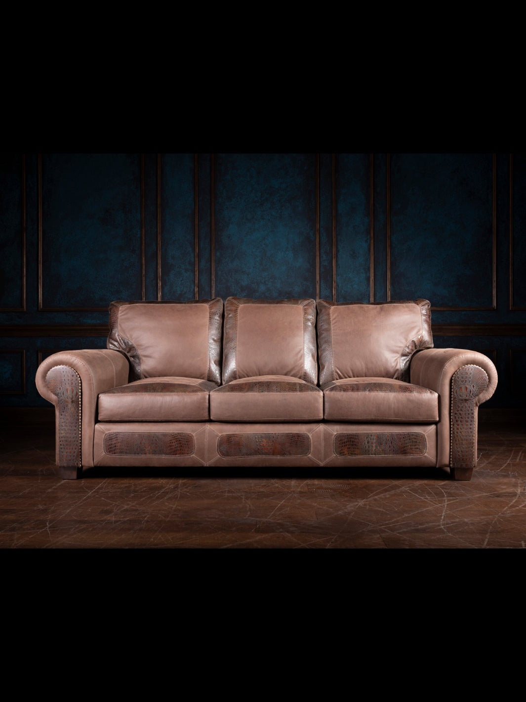 A brown leather sofa with rolled armrests and alligator-embossed leather accents, set against a dark paneled wall.