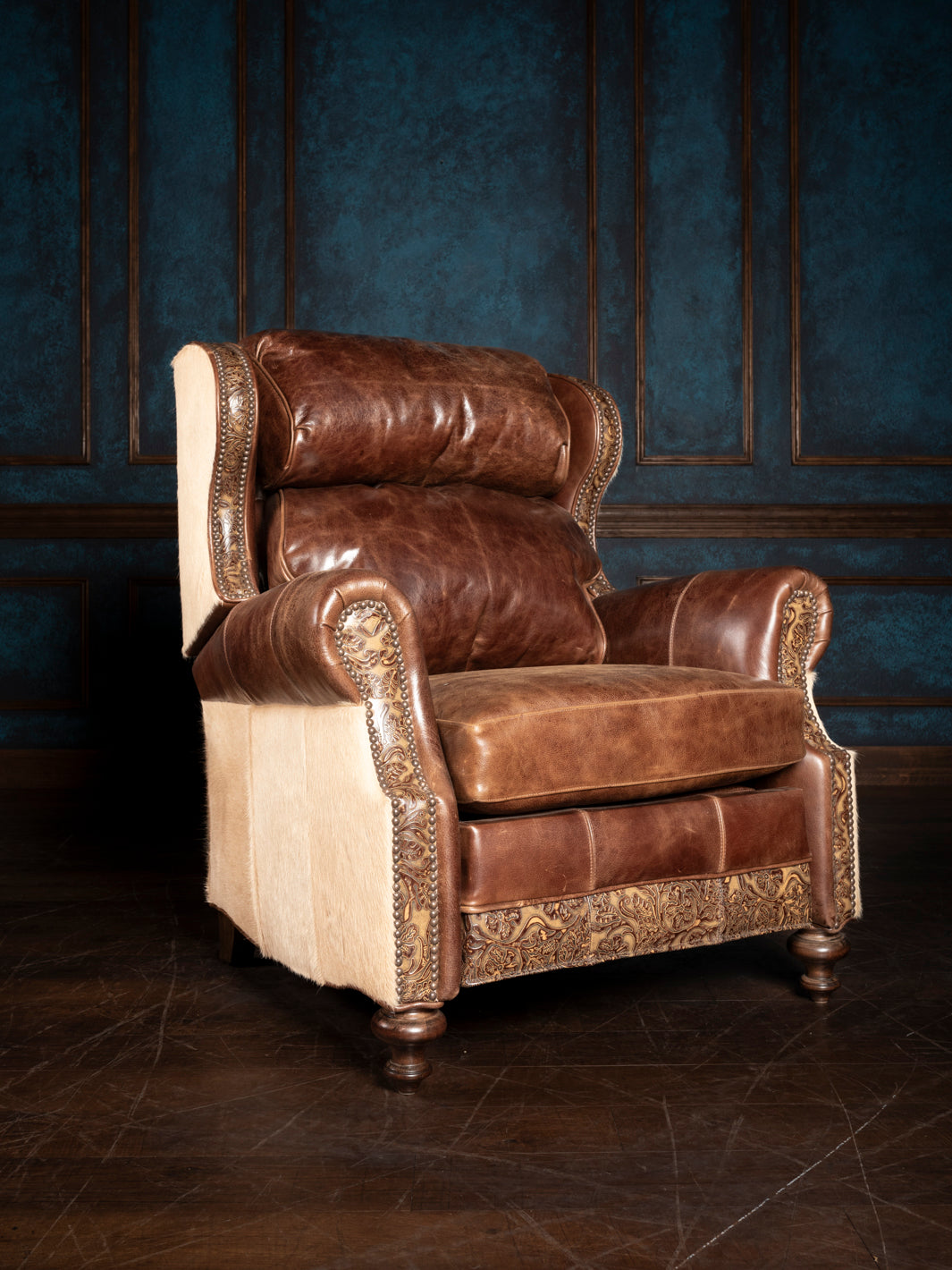 A luxurious Blondie Leather Recliner chair with brown leather and cowhide accents, featuring a traditional design with rolled arms and a pushback mechanism, set against a blue backdrop.