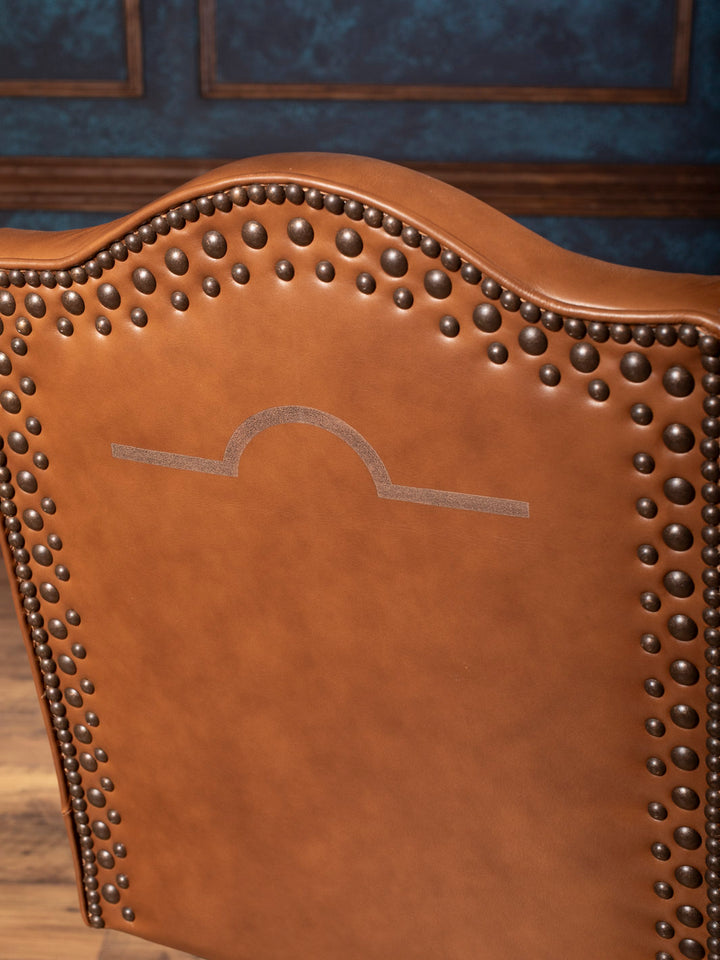 Brown leather chair with studded details against a blue wall.