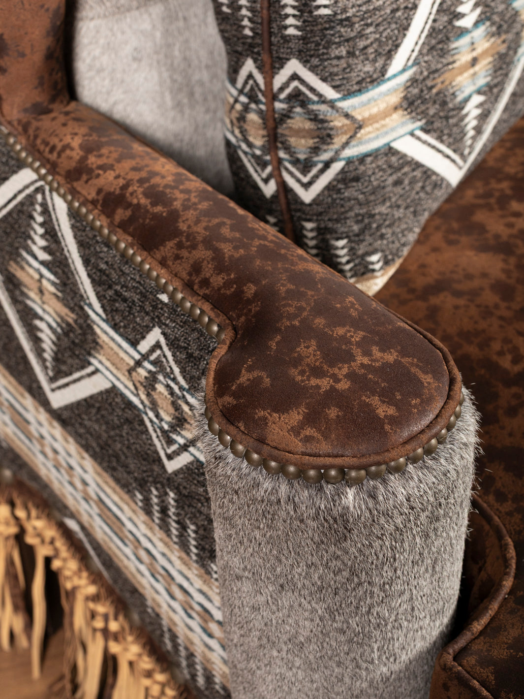 Armrest detail featuring nailhead trim, distressed leather, and tribal fabric