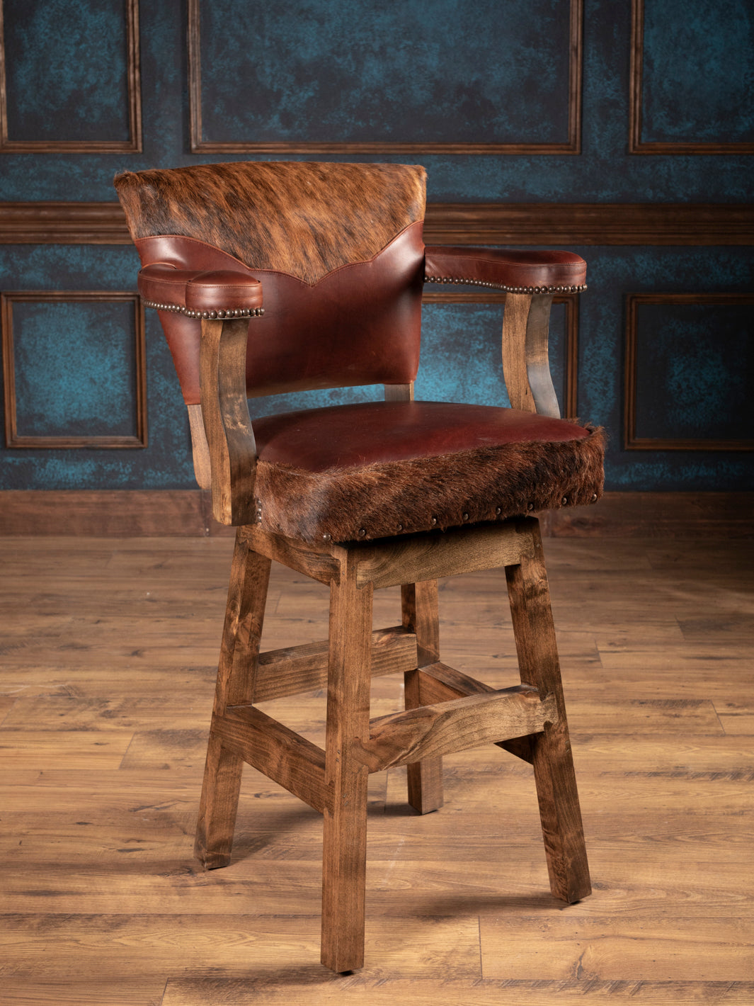 Wooden bar stool with brown leather seat and backrest against a dark blue paneled wall.