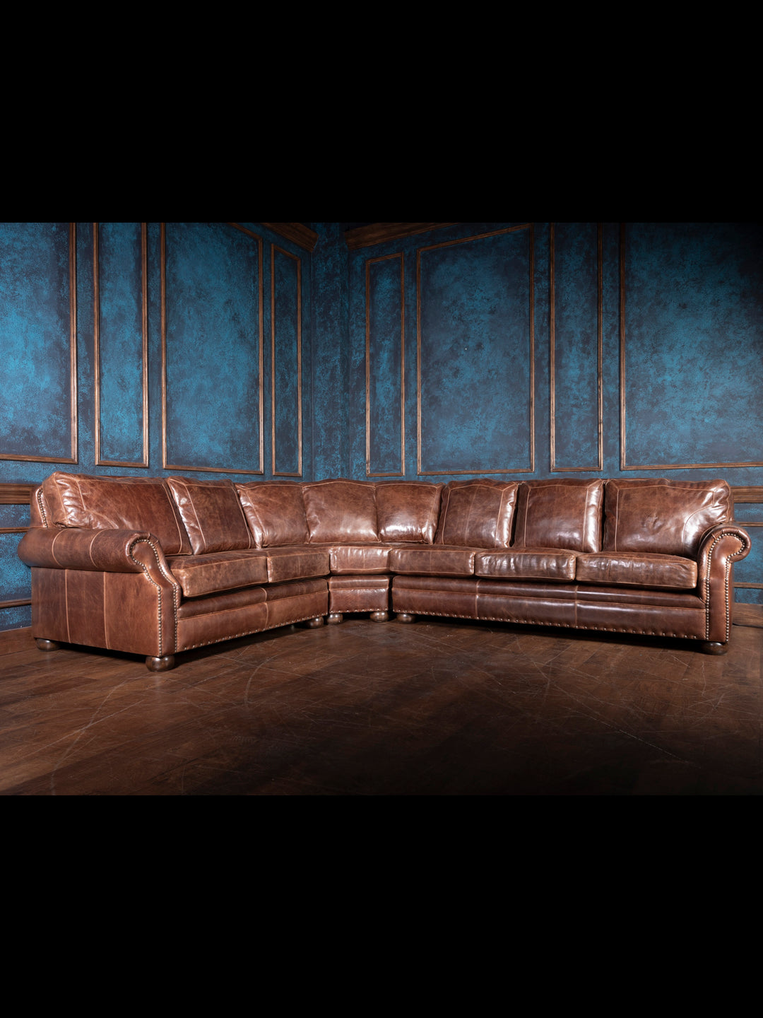 A large brown leather sectional sofa in a room with blue walls and wooden flooring.
