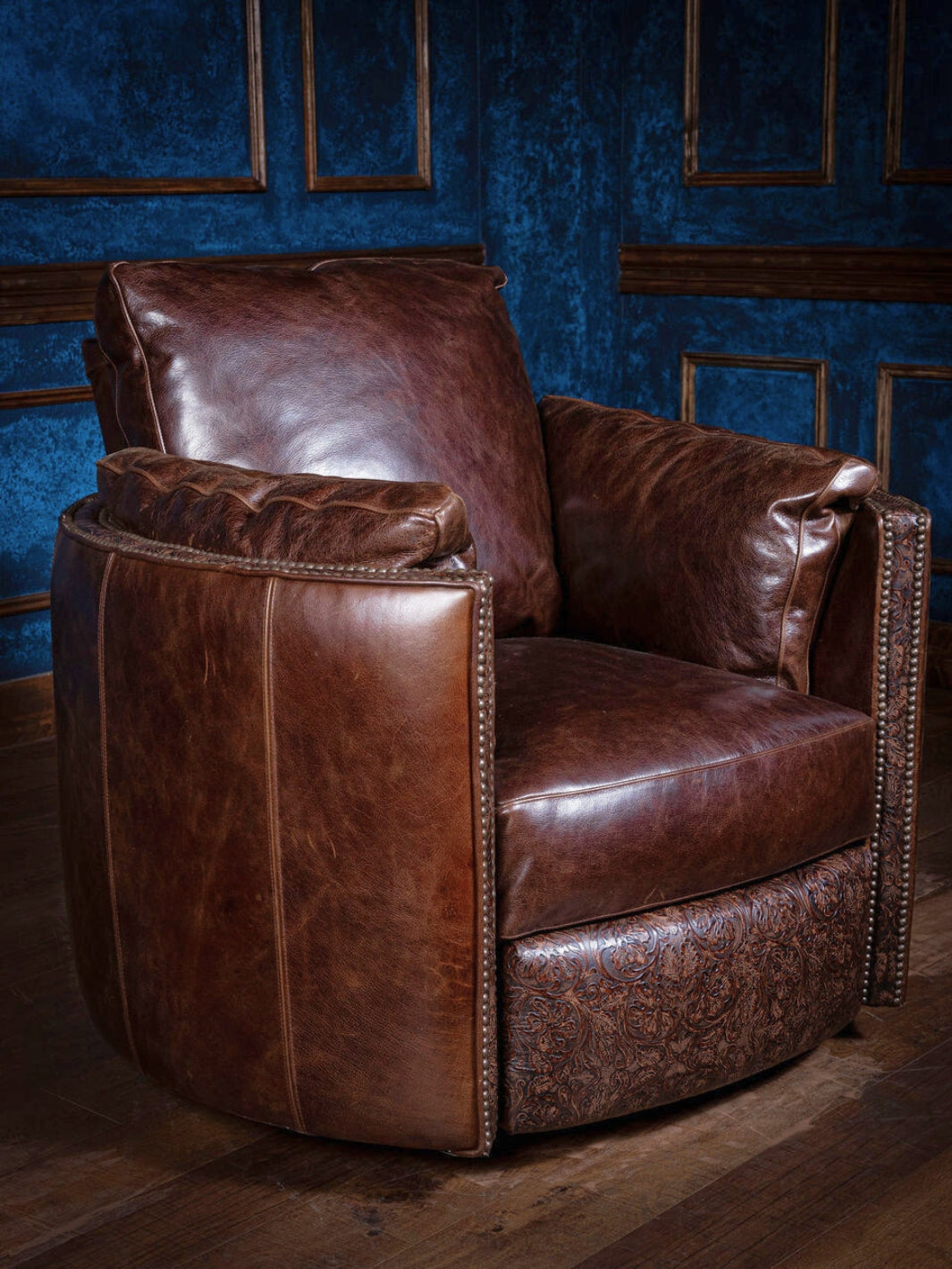 A brown leather snug swivel recliner chair placed on a wooden floor against a blue panelled wall.