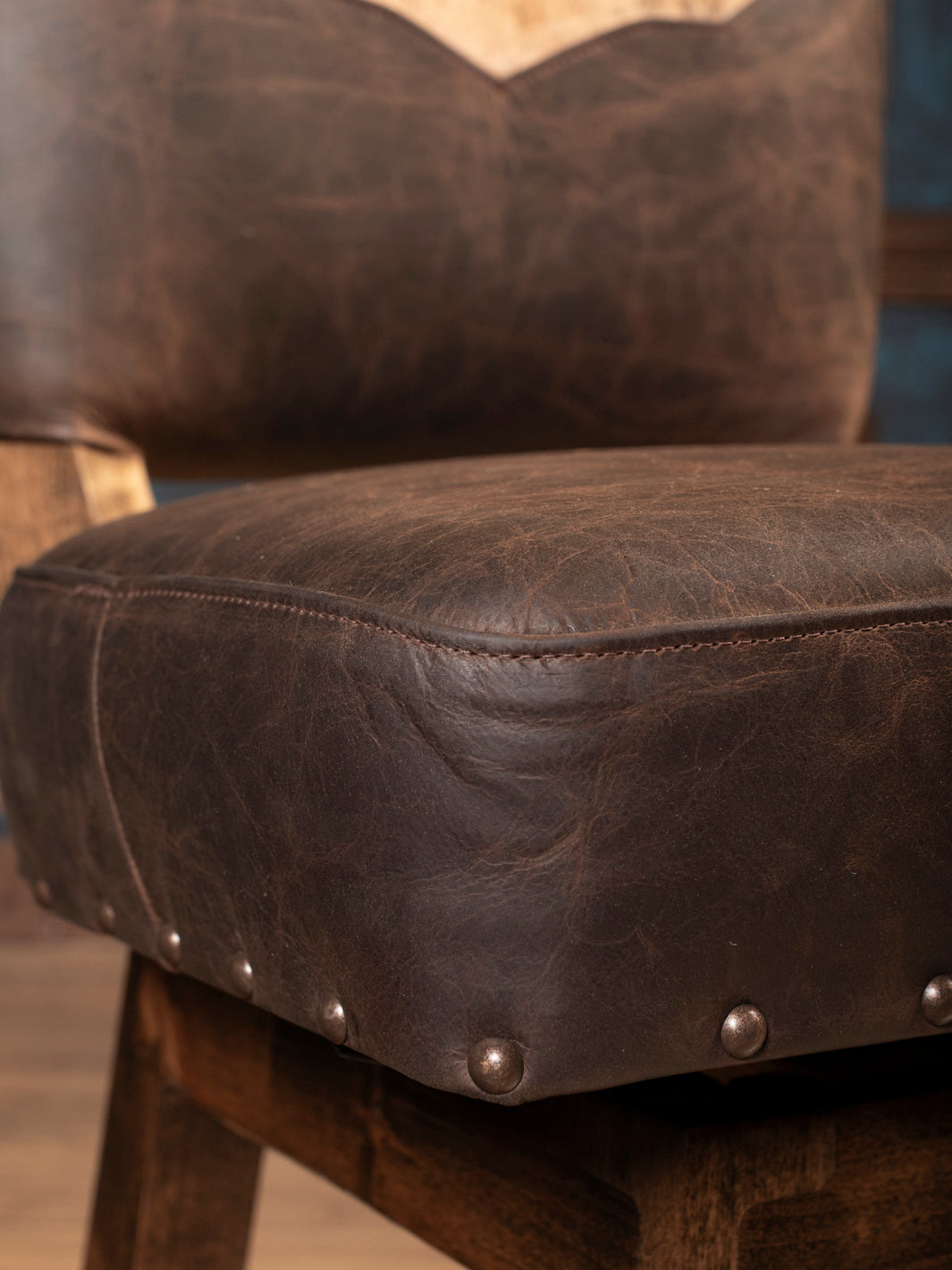 Seat Closeup: Brown full grain leather seat cushion with antique brass nailhead trim