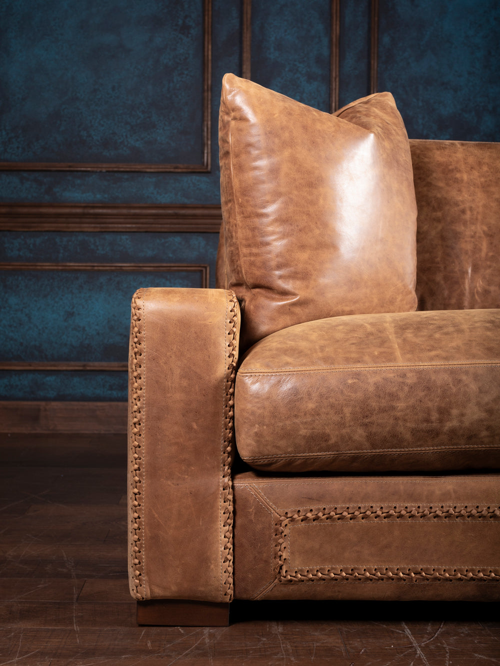 Side detail of a Western leather sofa showing thick seat cushions and stitched armrest accents.