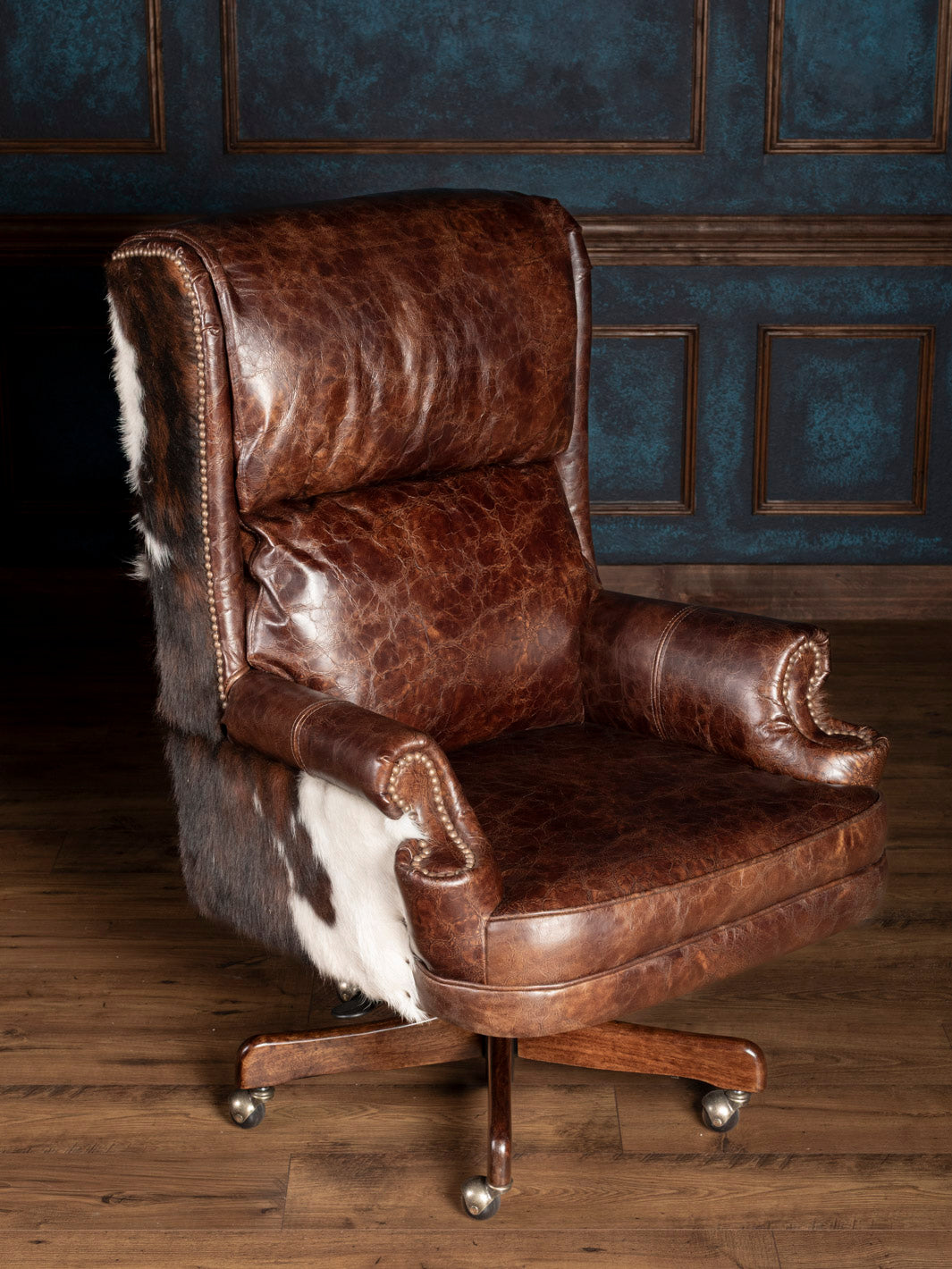 A brown executive leather desk chair with cowhide accents, featuring a high backrest, armrests, and a five-star base with casters.
