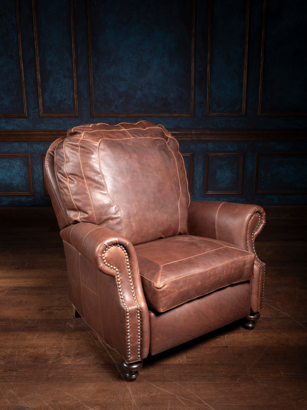 A brown leather recliner with a framed stitch design, positioned in a room with blue paneling.