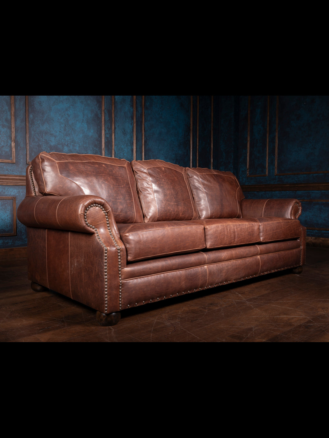 Angled side view of the Red Oak leather sofa showcasing the full grain texture, rolled arms, and plush back cushions against a navy paneled wall.