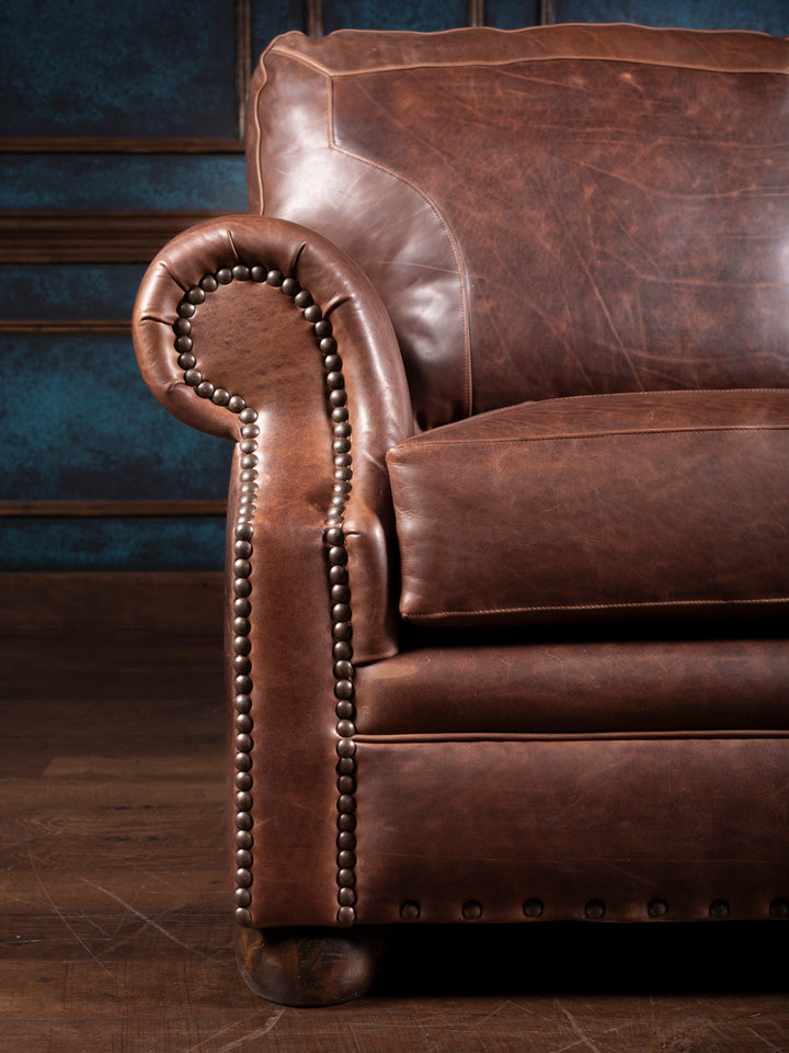 Close-up detail of the leather sofa’s rolled arm with nailhead accents and visible creases that highlight the rich, durable Red Oak leather.