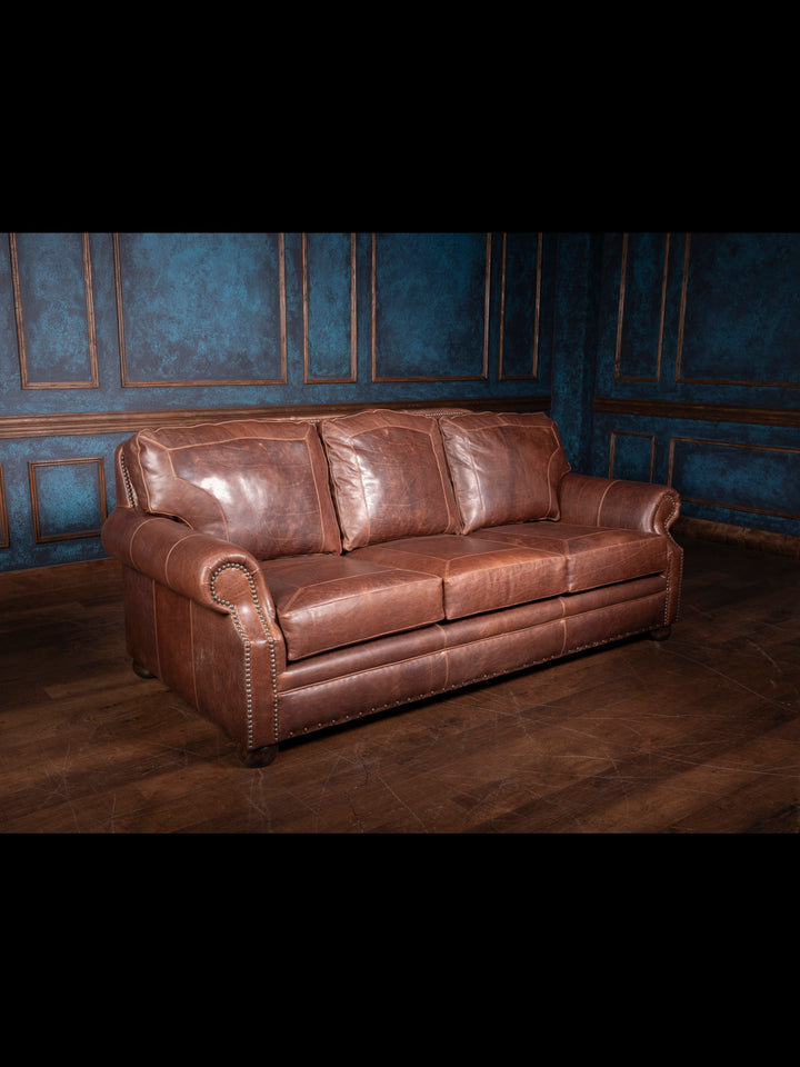 Angled wide view of the full Western leather sofa, displaying its classic silhouette, generous cushioning, and rustic hardwood legs.