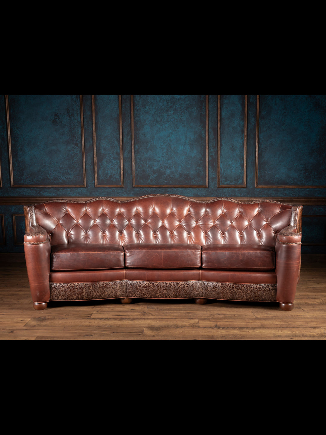 A honey-toned leather sofa with tufted backrest and embossed leather detailing, set against a blue panelled wall.