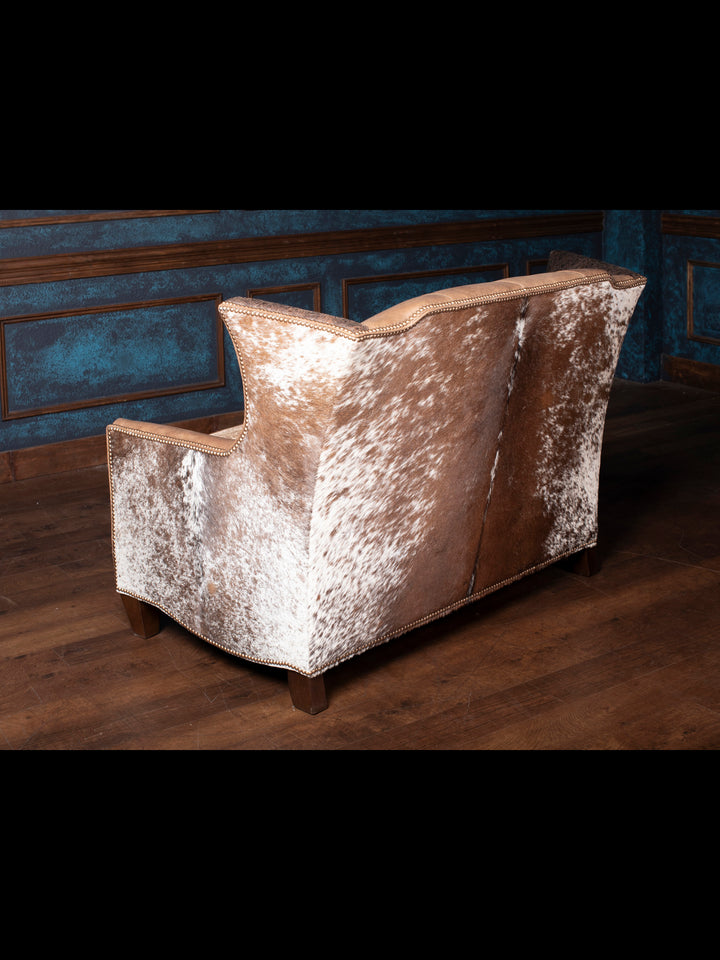 Back view of the Hazelnut Leather Settee, highlighting the distinctive hair-on-hide accents and solid wood legs, perfect for rustic or Western interiors