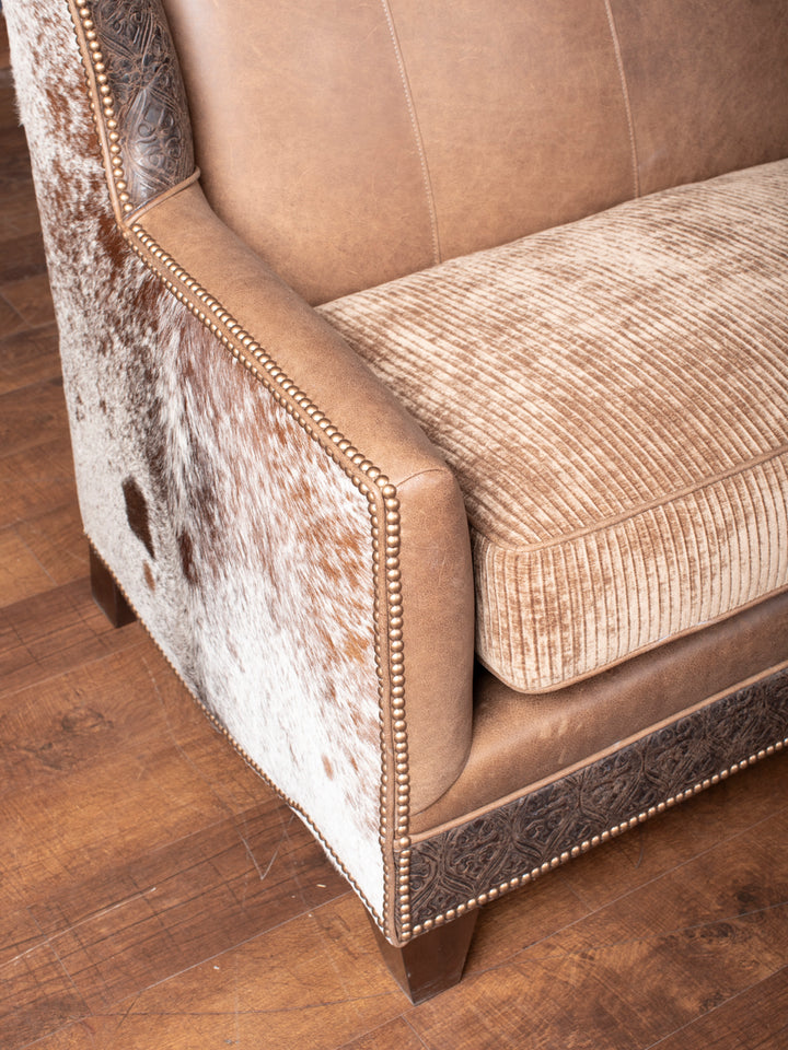 Close-up of the arm of the Hazelnut Leather Settee, featuring fine stitching on the Rustler leather and elegant brass nailhead trim.
