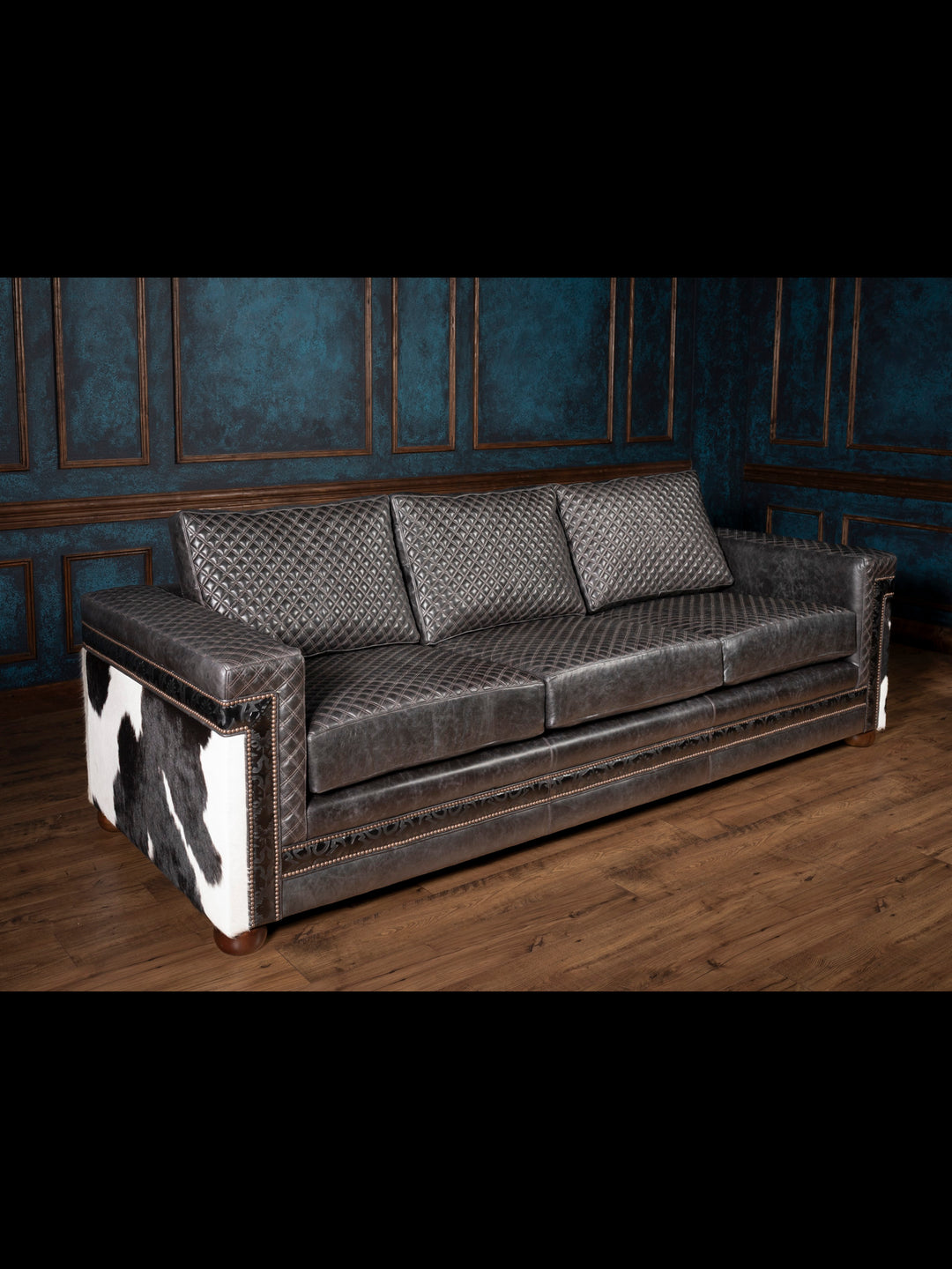 Angled view of black quilted leather sofa with black and white cowhide accents on outside arm.