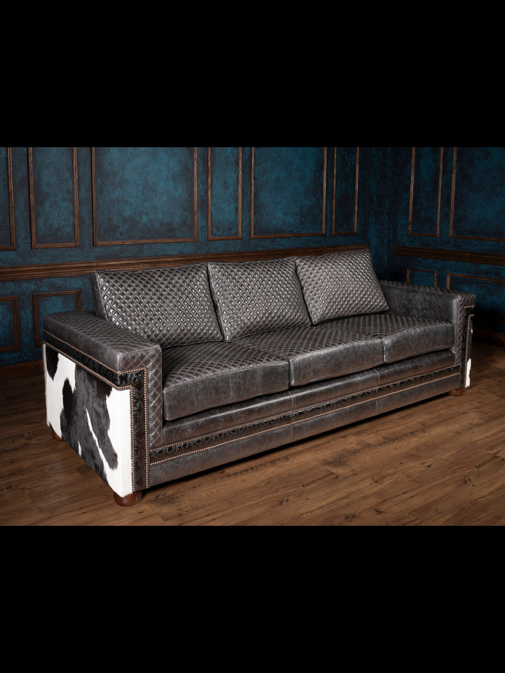 Angled view of black quilted leather sofa with black and white cowhide accents on outside arm.