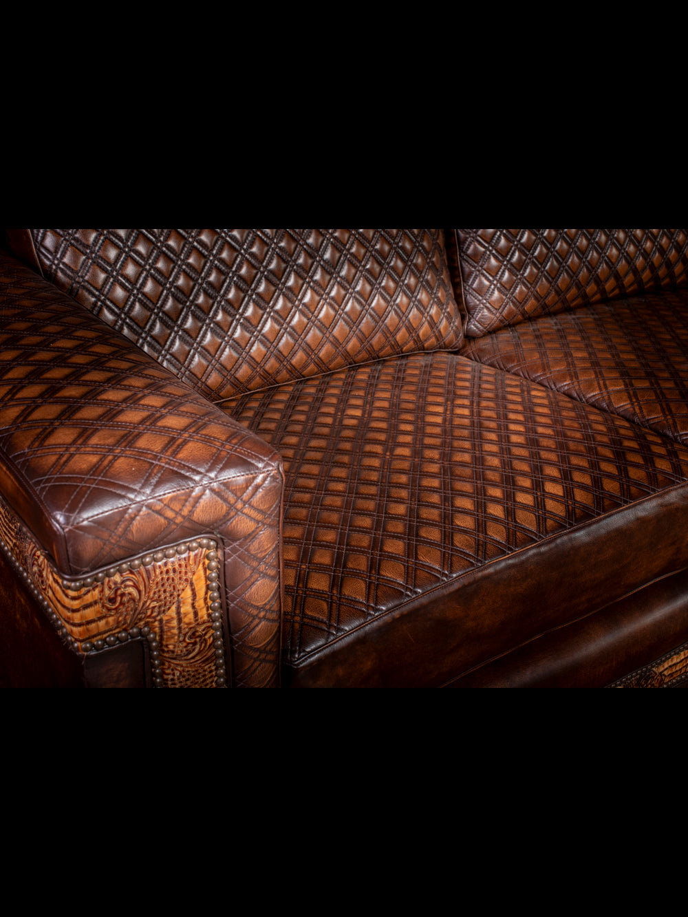 Close-up of the quilted leather seat and armrest with intricate embossed leather trim and brass nailhead accents on a rustic western leather sofa.