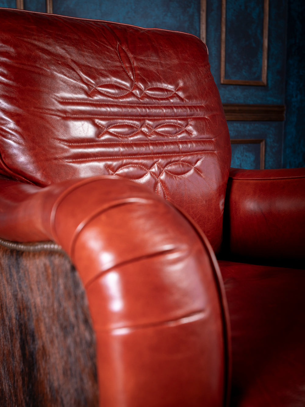 Detail view of a western-style luxury chair with smooth leather armrest, visible saddle stitching, and a cowhide side panel framed by nailhead trim for a refined rustic look.