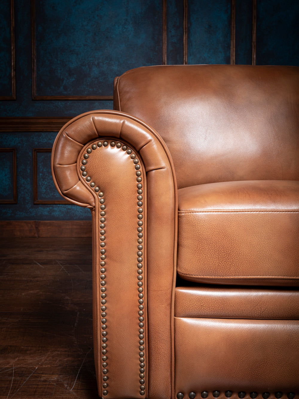 Close-up view of the chair’s rounded armrest, showcasing detailed brass nailhead trim and the natural grain of the leather upholstery.
