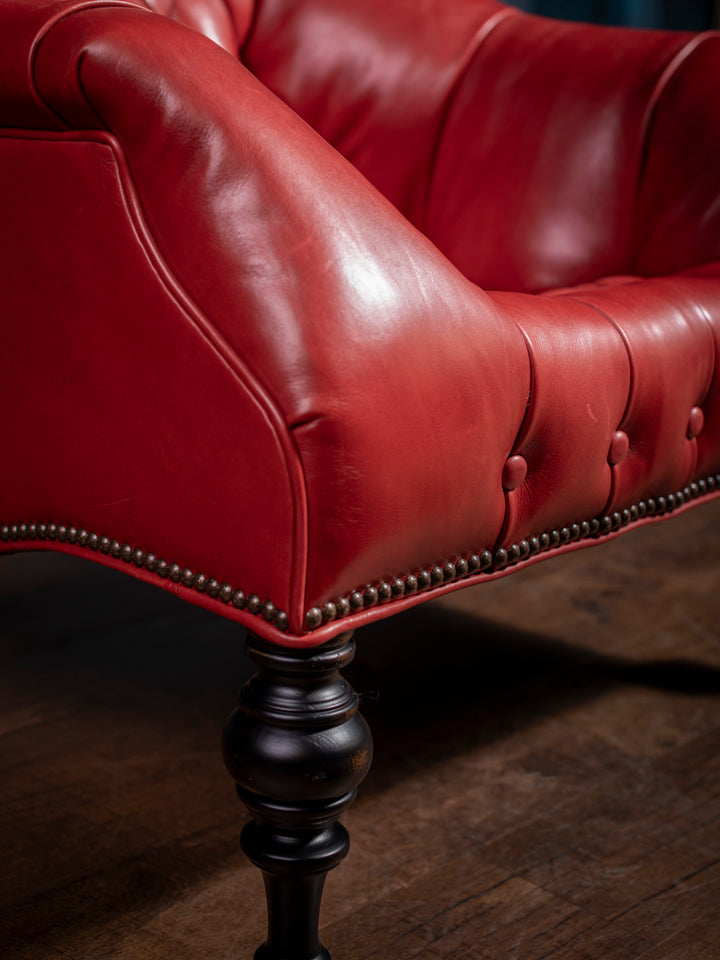 Close-up of turned black wooden leg and antique nailhead trim on a handcrafted red leather accent chair, showcasing Western elegance and durable construction.
