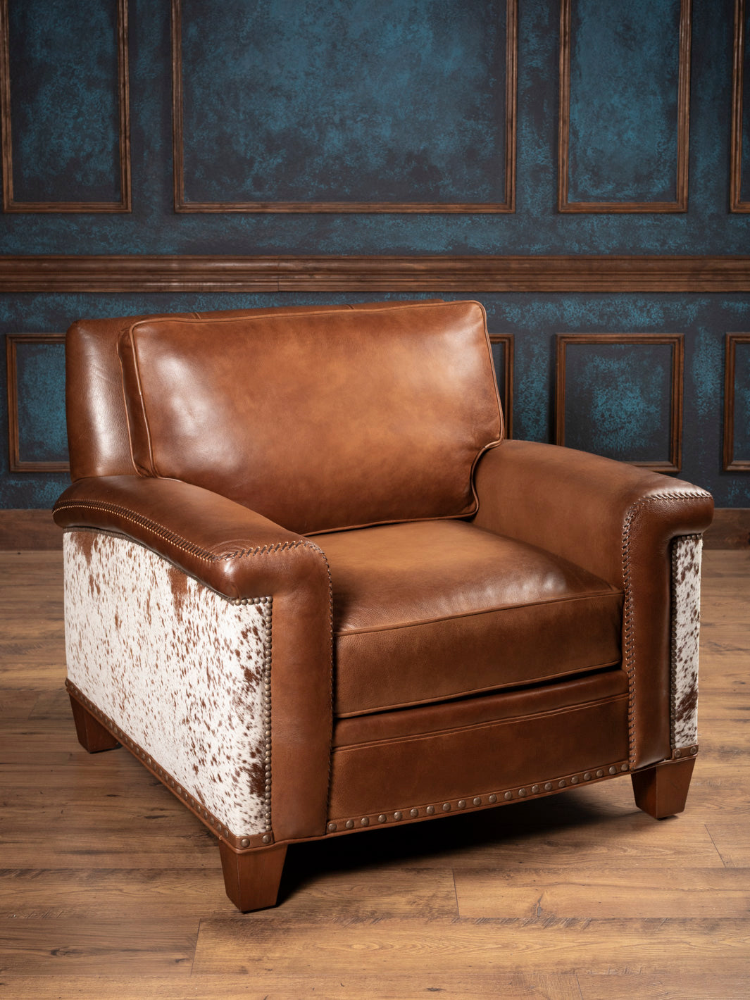 Brown leather armchair with patterned armrests against a blue paneled wall.