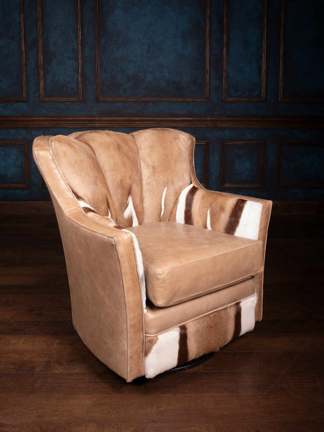 A brown leather swivel chair with a plush seat cushion and barrel style back, featuring exotic springbok deer hide accents.
