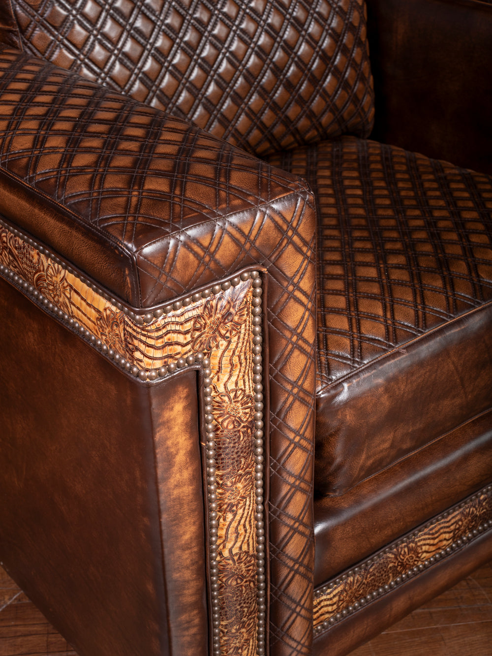 Close-up of the Rodeo Architect leather chair showcasing intricate crosshatched quilting, floral tooled leather border, and bronze nailhead accents along the arm and base.