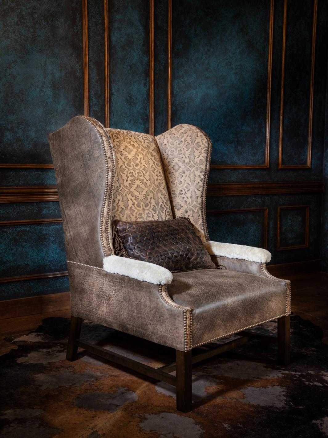 Western high-back accent chair with a sculpted wingback silhouette, featuring distressed taupe upholstery, embroidered back panel, sherpa-trimmed arms, and nailhead trim along the frame.
