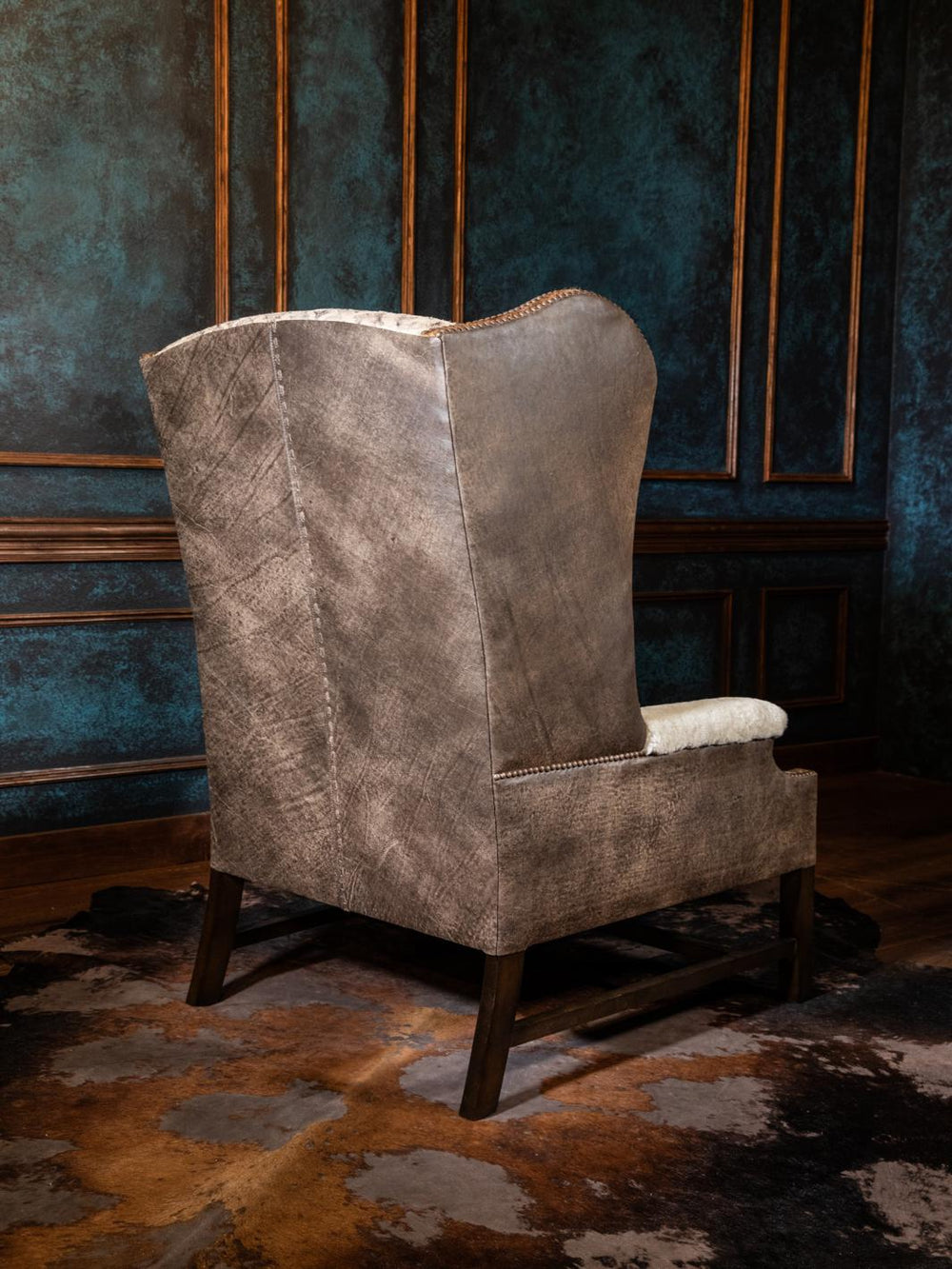 Backside of a tall Western wing chair upholstered in a weathered gray fabric with subtle texture and wooden leg frame, ideal for rustic cabin or lodge interiors.
