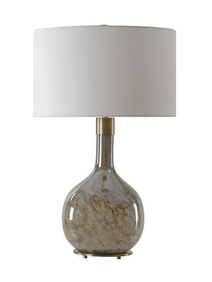 A decorative table lamp with a rounded glass base featuring swirling earthy tones of beige and brown, topped with a white fabric drum shade and a brass accent near the neck
