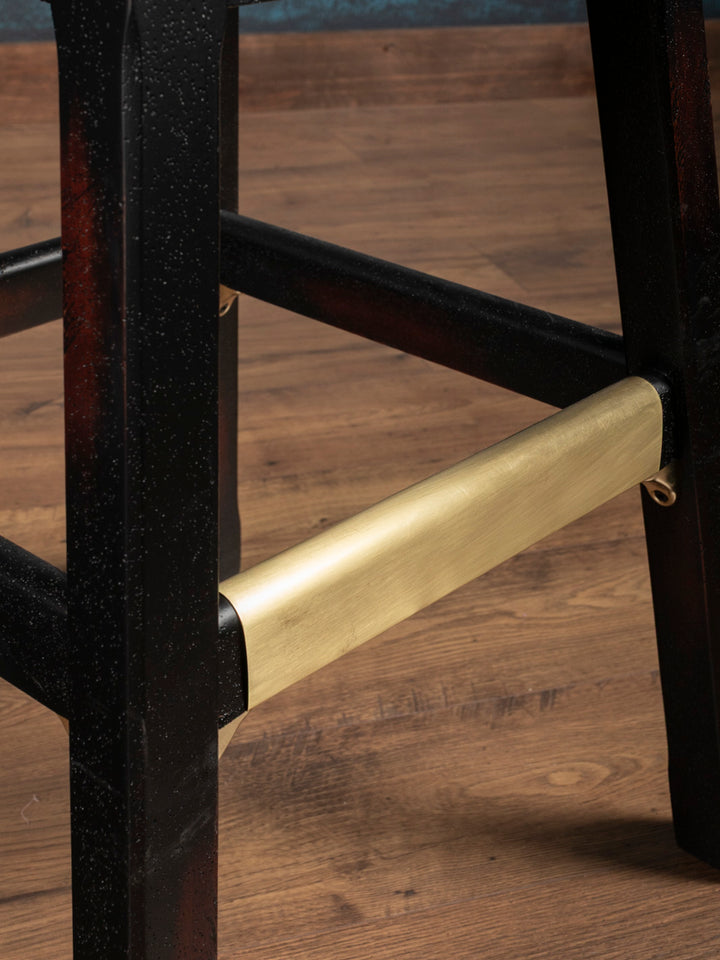 Close-up of brass-covered footrest and distressed wood legs on Sedona Saddle Leather Bar Stool