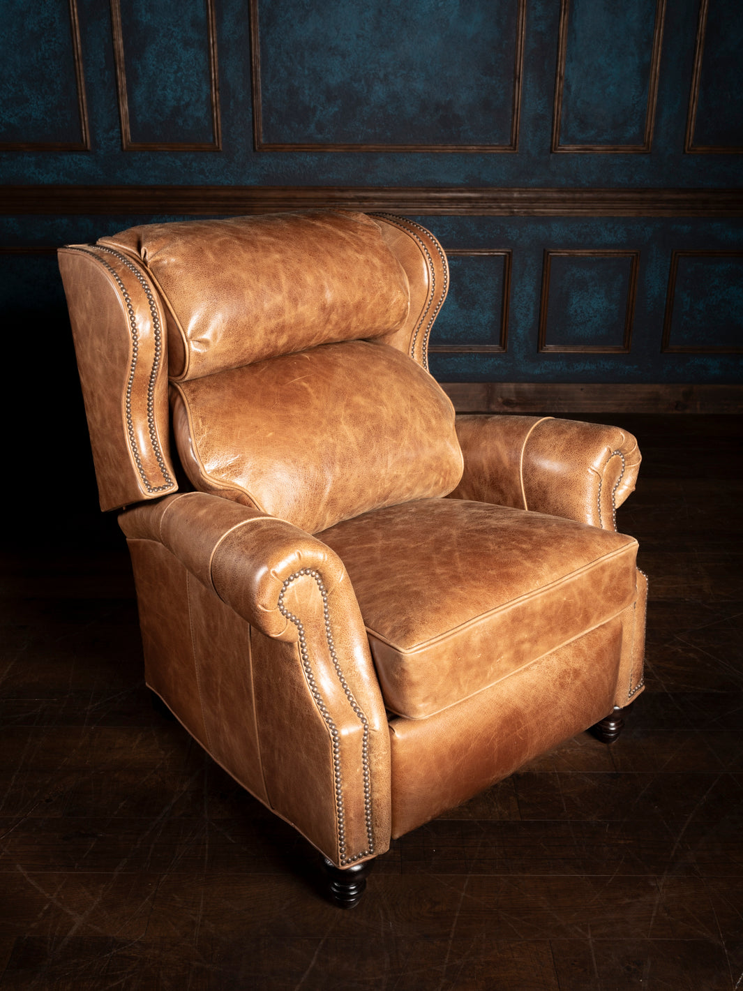 A brown leather recliner chair with nailhead trim, situated in a room with panelled walls.