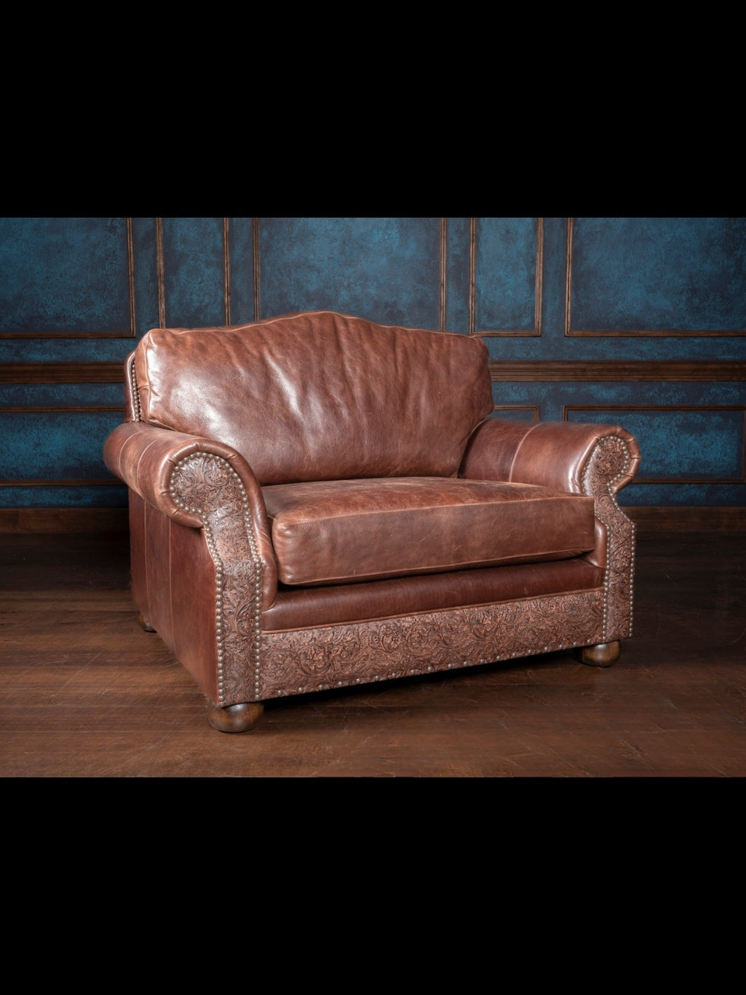 Oversized Texas leather armchair with a scalloped back, rolled arms, and deeply cushioned seat, framed with embossed leather panels and bun feet.