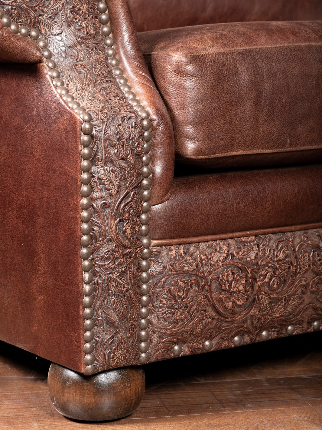 Close-up of floral tooled leather panel and nailhead trim along the base and leg of a Texas leather chair, showcasing artisan craftsmanship