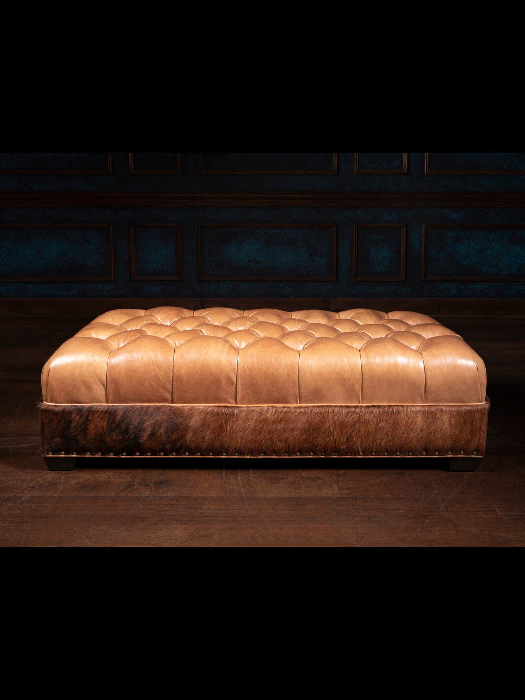 A tufted rectangular brown leather ottoman with a hair-on-hide texture.