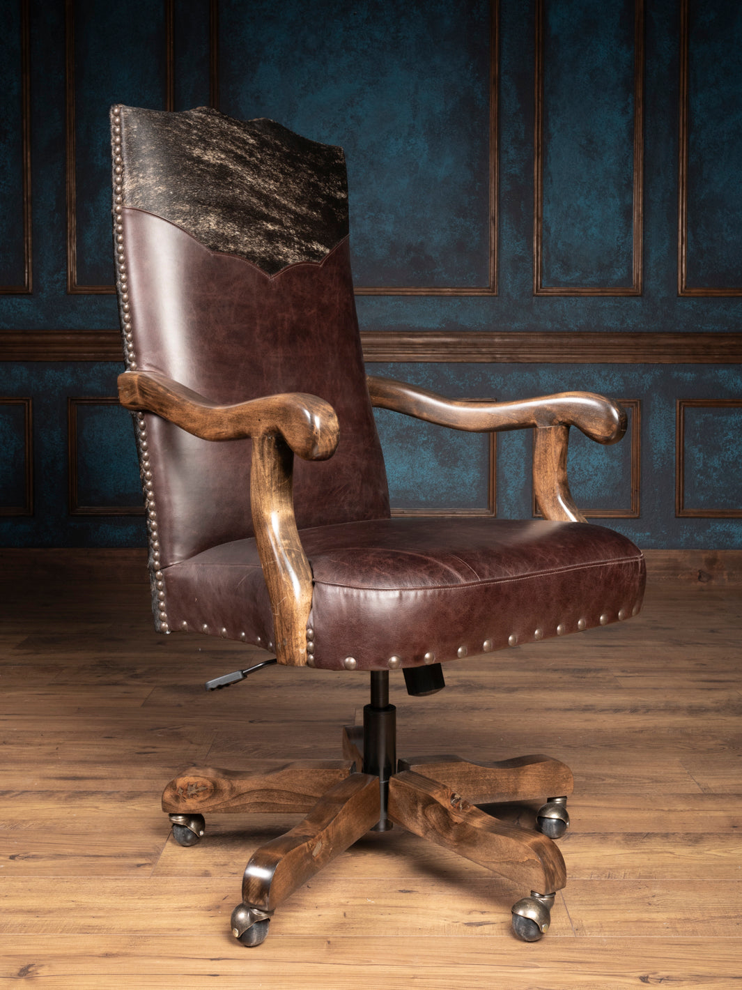 A dark leather desk chair with a natural cowhide accent back and wooden arms and base, featuring a high backrest and ergonomic design.