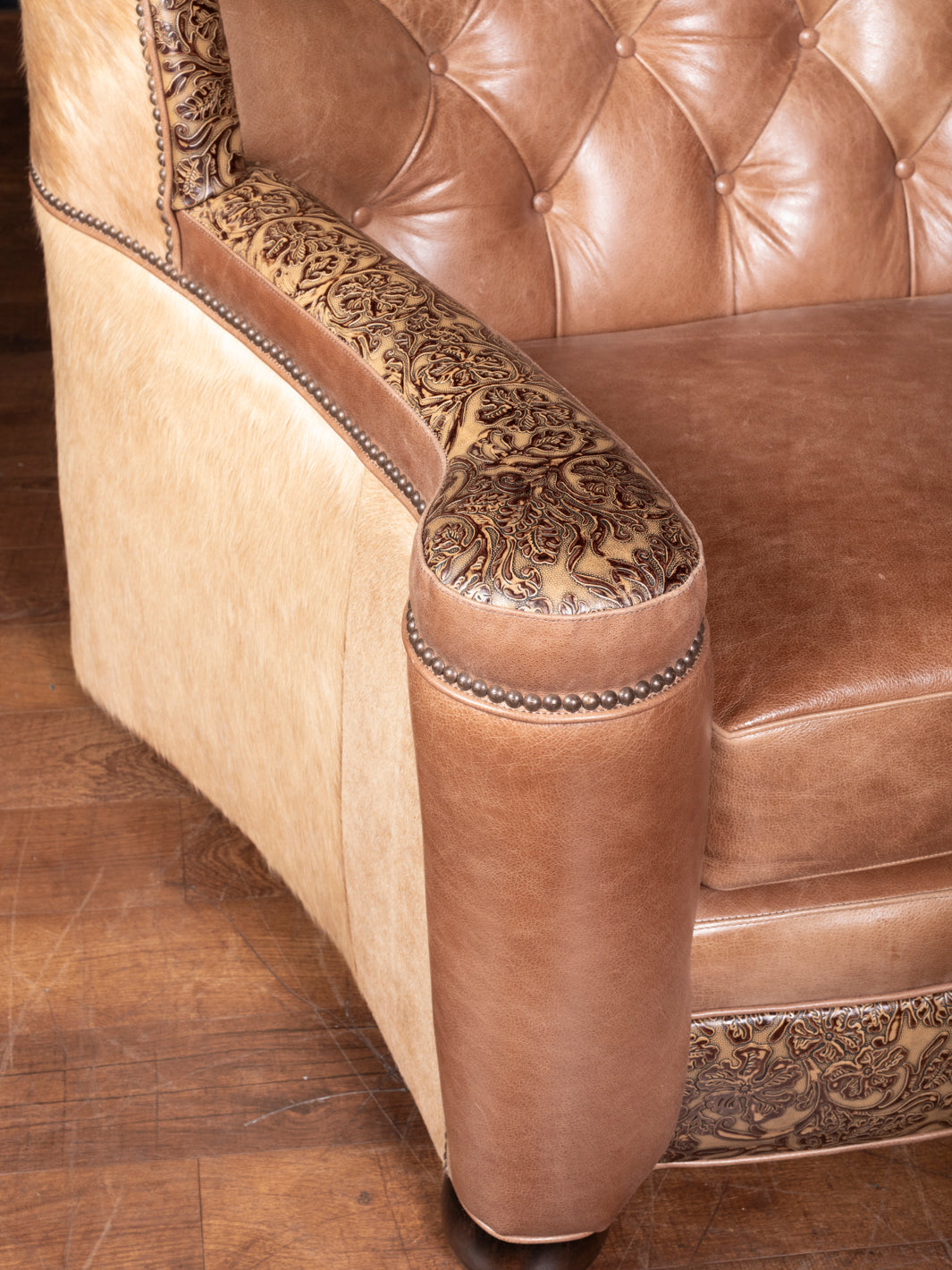 Close-up of Western-style leather sofa armrest featuring hand-tooled sunflower embossing and cream hair-on-hide panels.