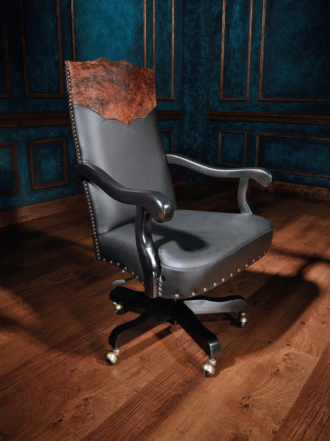 A black leather desk chair with a brindle yoke detail, set against a wooden backdrop with uplighting.