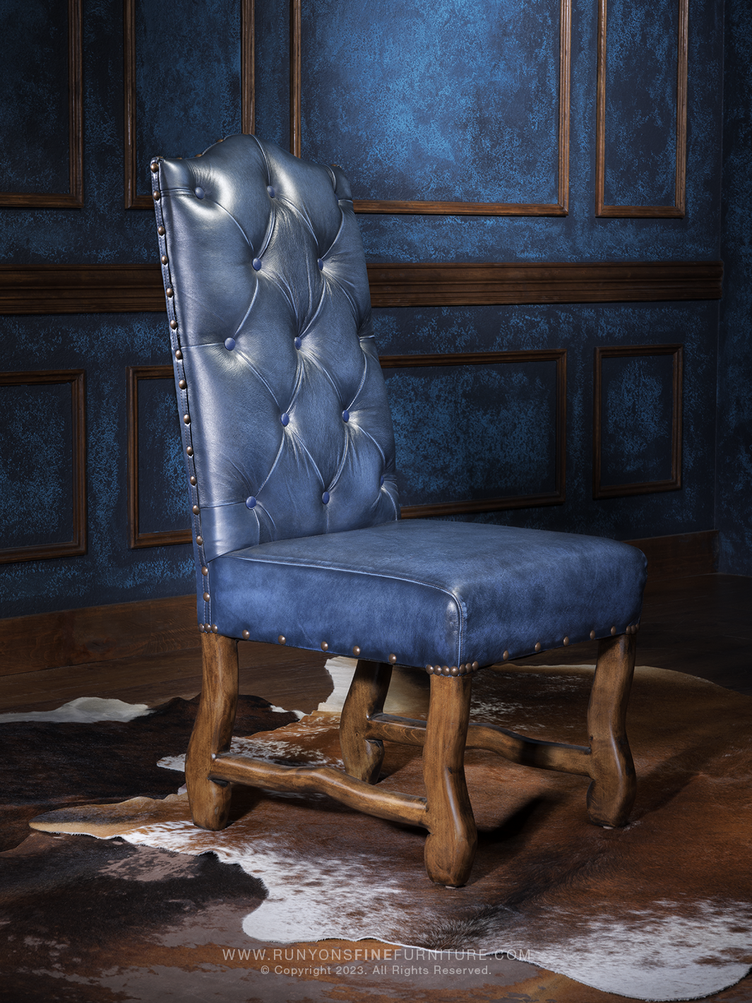A blue leather side chair with a tufted backrest and nailhead trim, placed against a blue textured background.