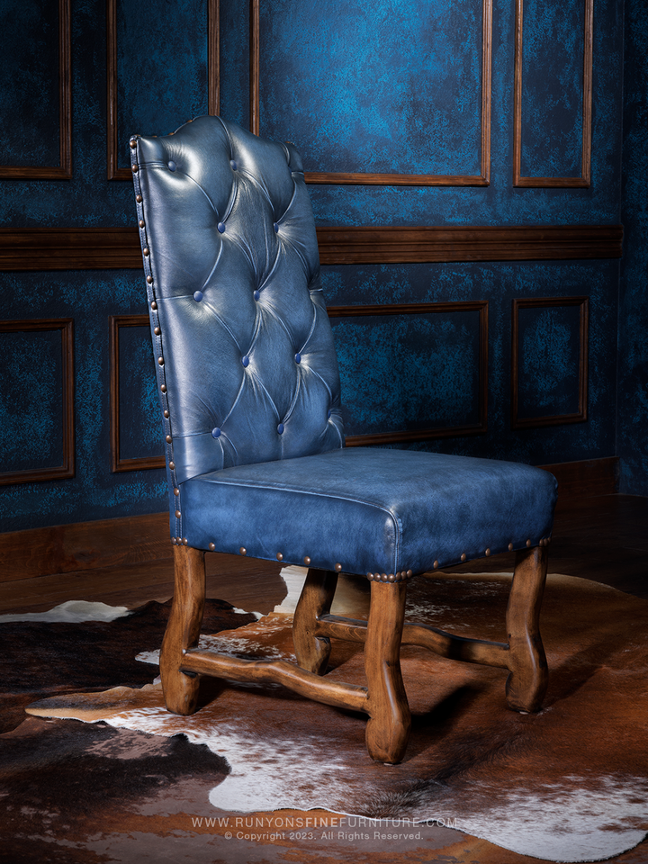 A blue leather side chair with a tufted backrest and nailhead trim, placed against a blue textured background.