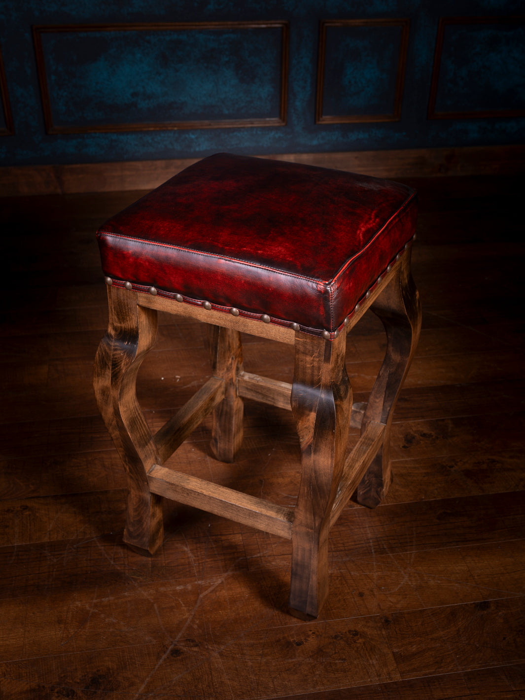 A red leather saddle stool with a burnished finish, featuring a wooden frame and a padded seat.