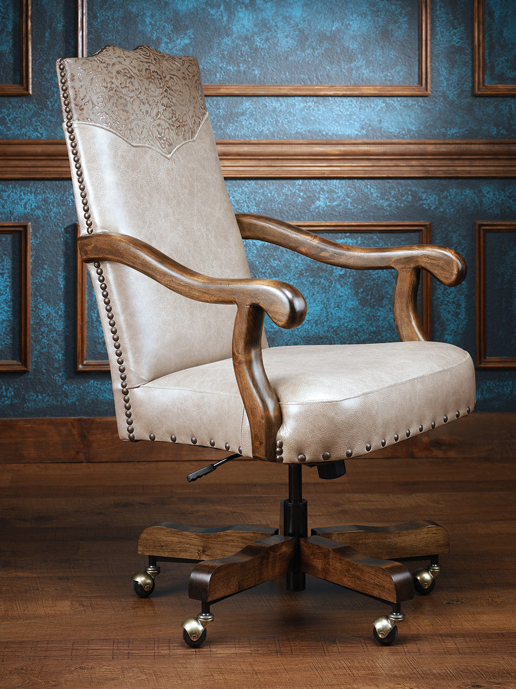 A classic cowgirl desk chair with a beige upholstered backrest and seat, featuring a wooden frame and embossed leather details, mounted on a five-star base with caster wheels.