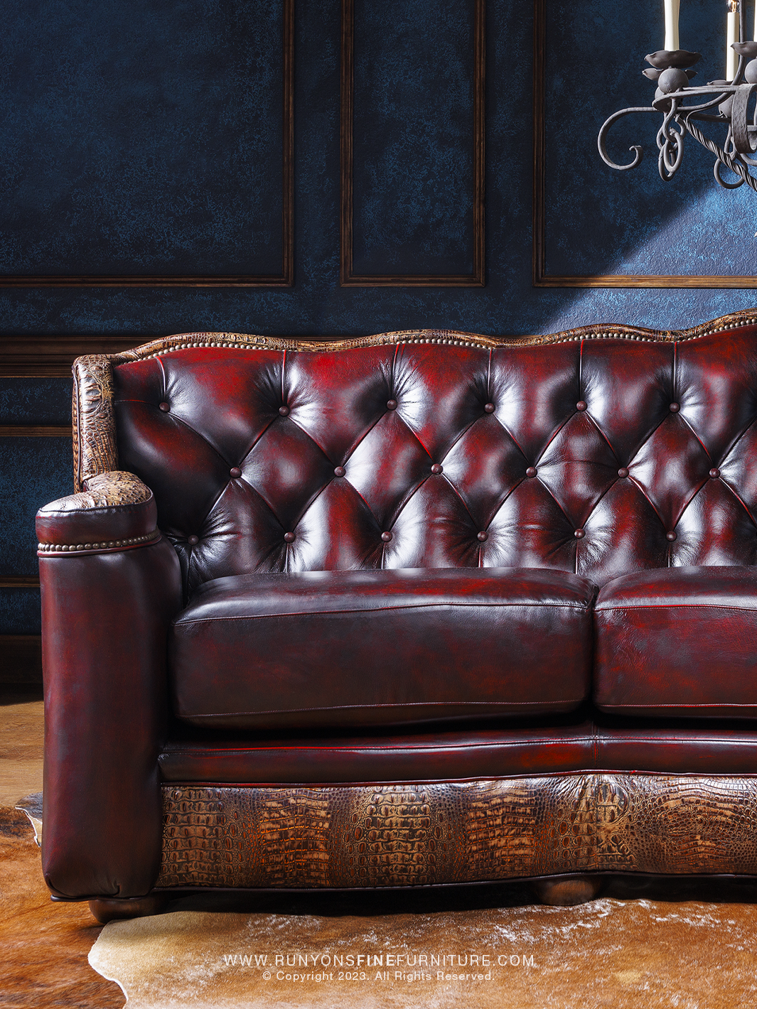 A red leather sofa with tufted buttons and crocodile brown embossed accents, placed in a room with blue walls and a chandelier.