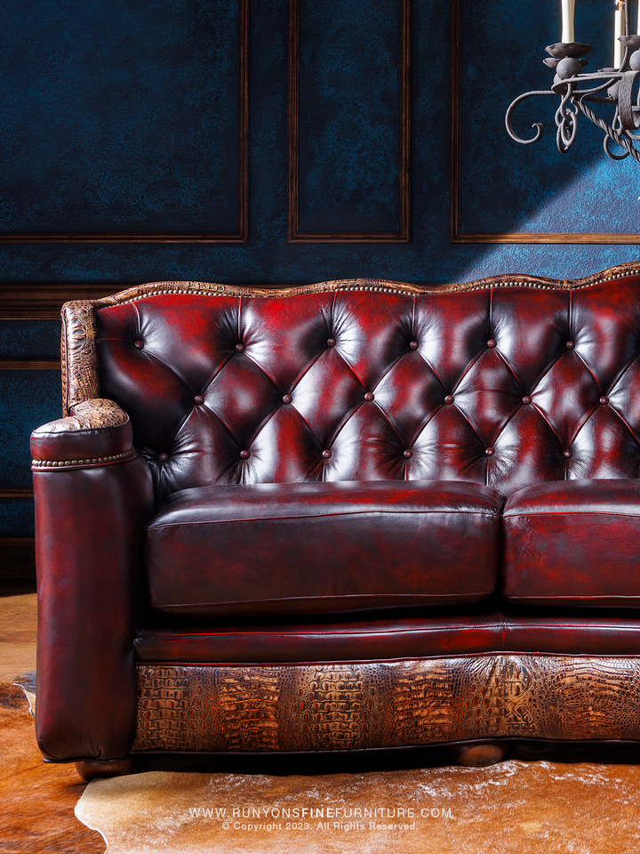 A red leather sofa with tufted buttons and crocodile brown embossed accents, placed in a room with blue walls and a chandelier.