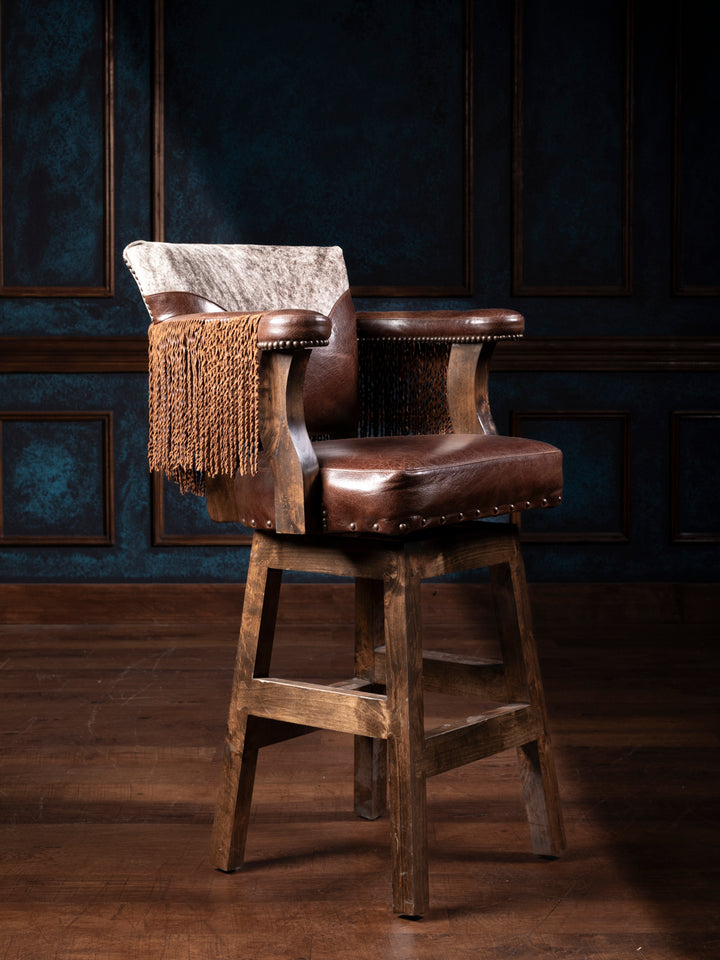 A brown leather bar stool with a fringe pull-up effect on the backrest, situated in a room with dark walls.